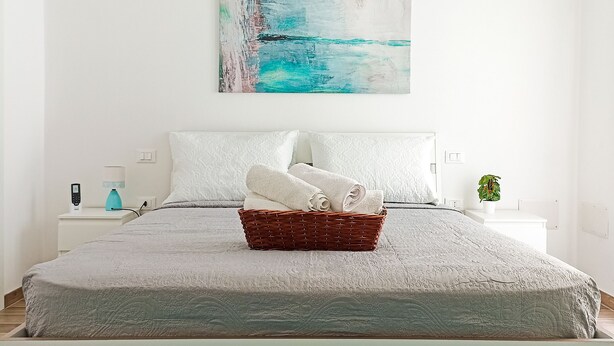 A bedroom with a bed, a nightstand, a lamp, a painting, and a plant. - Kolossoi Guest House (Cabras)