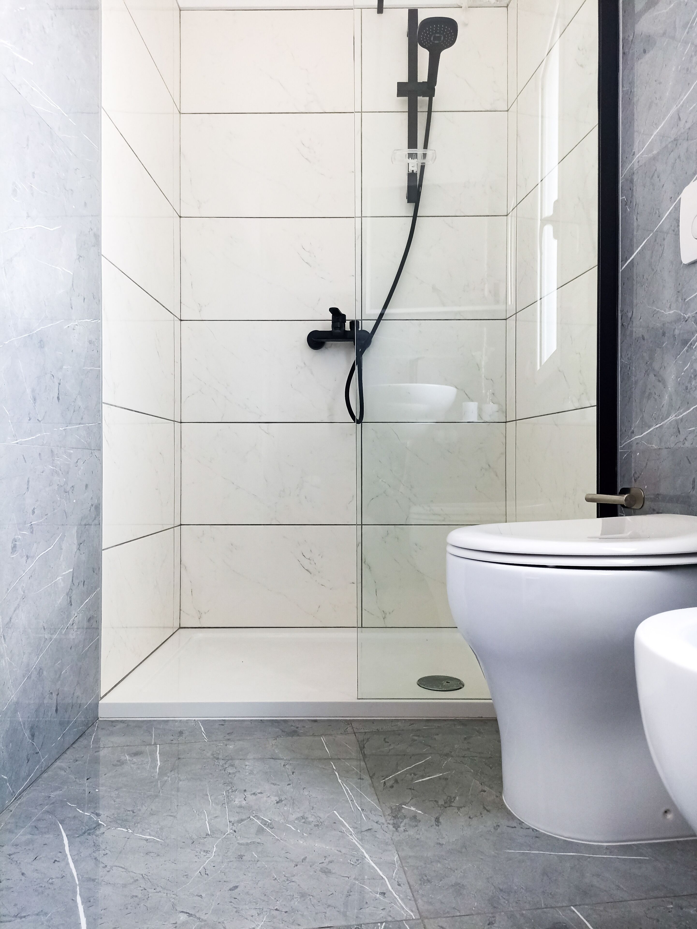 Ein modernes Badezimmer mit einer Glaskabine zur Dusche, einer weißen Toilette und einem Marmorboden.