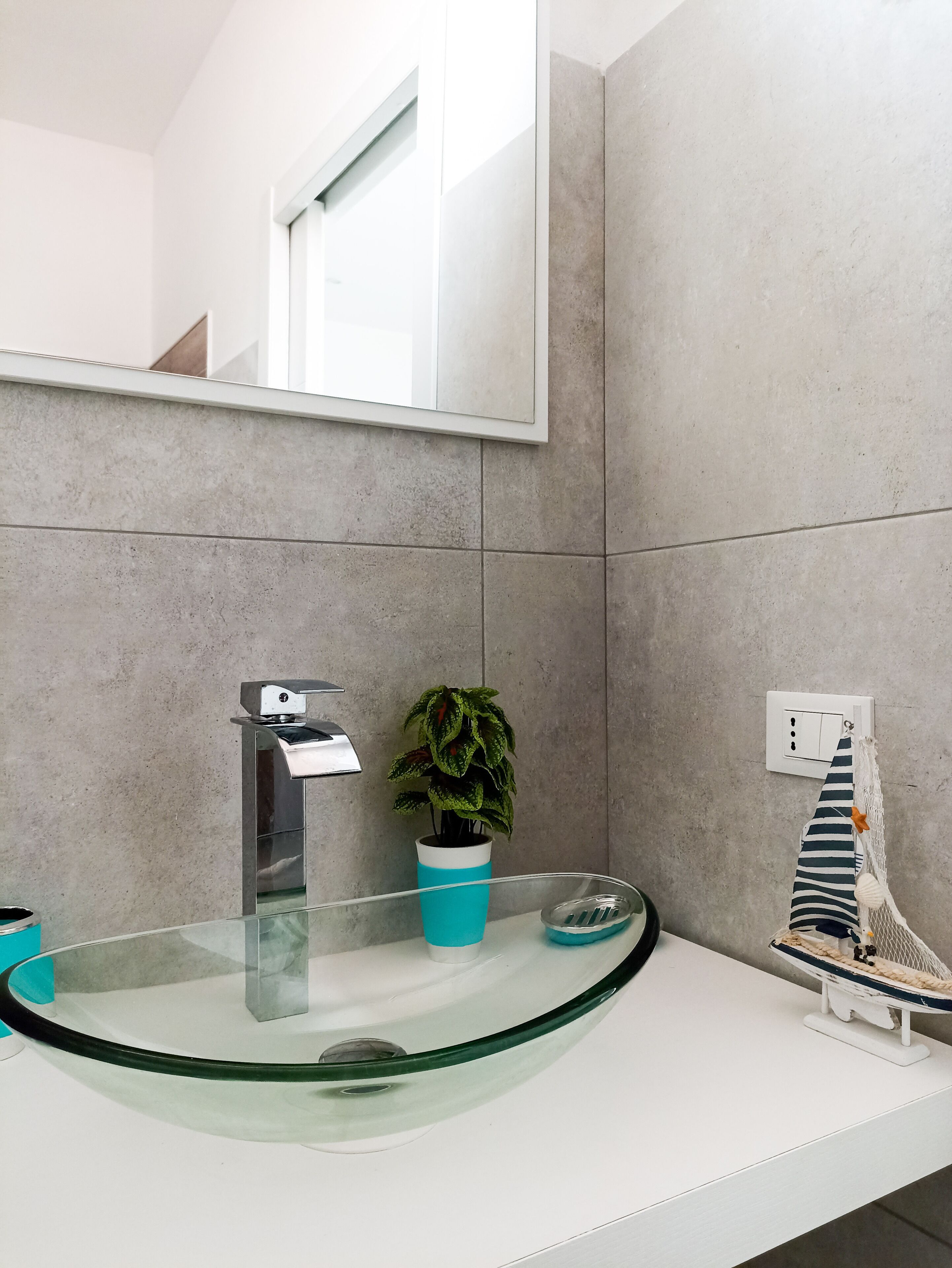 Une salle de bain moderne avec un lavabo en verre, une plante en pot et une maquette de bateau décorative.