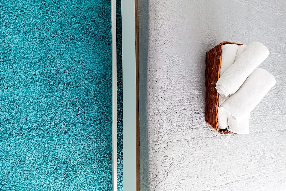 A corner of a room with a teal carpet and a white textured wall.