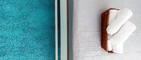 A corner of a room with a teal carpet and a white textured wall.