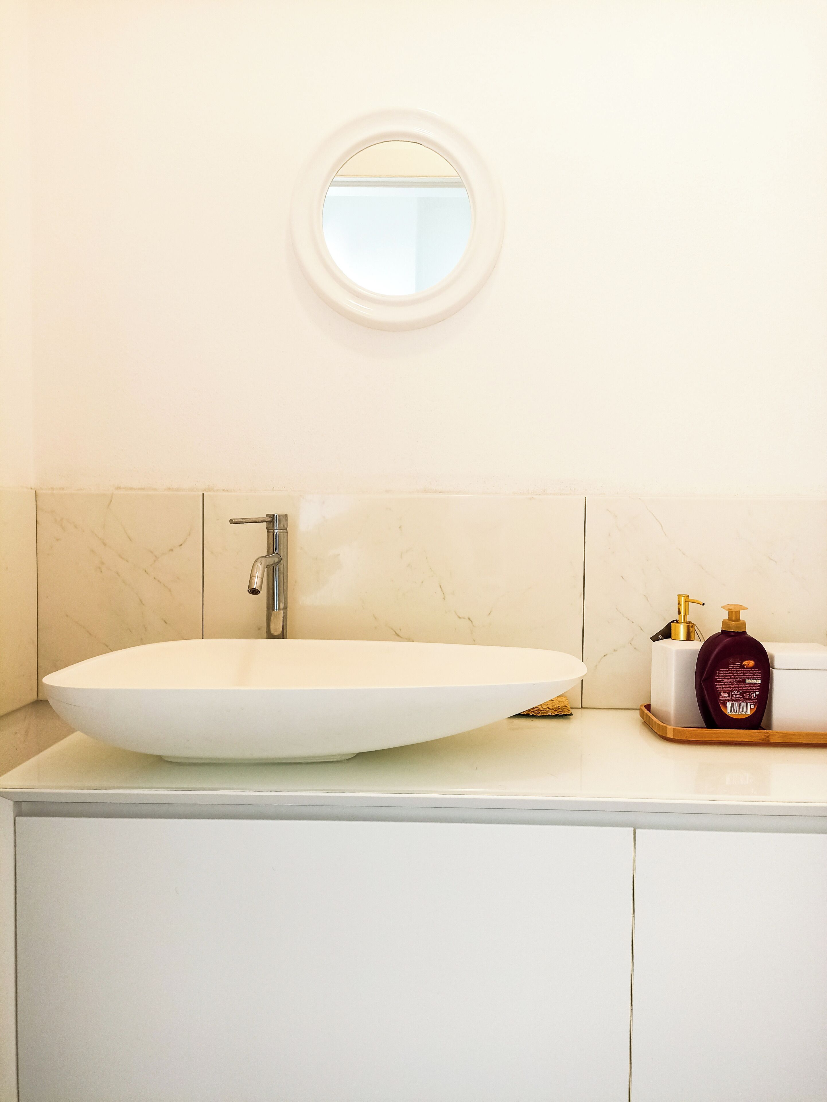 Une salle de bain avec un grand lavabo ovale, un miroir rond et une bouteille de shampoing posée sur le comptoir.