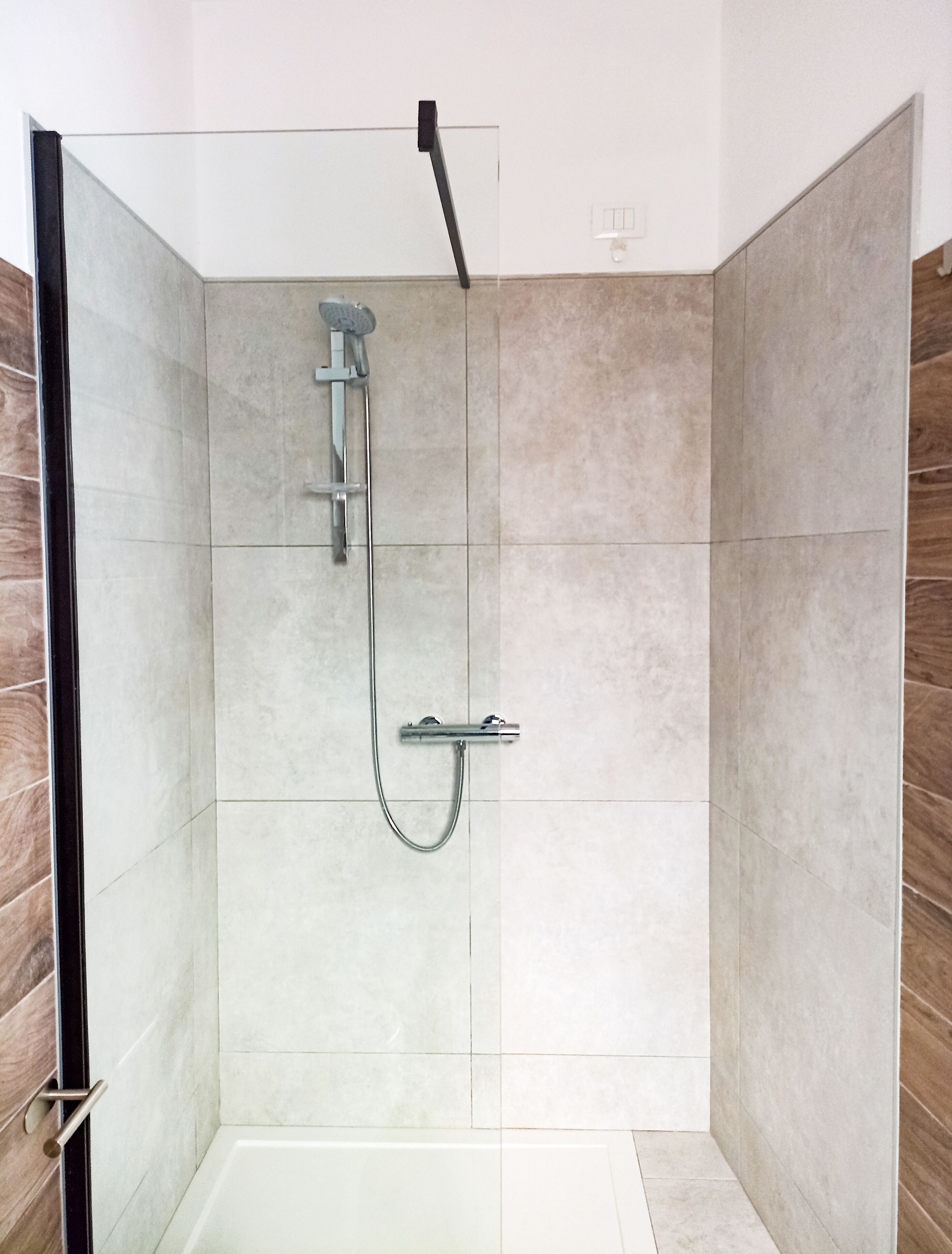 A modern shower with a handheld showerhead and a fixed showerhead, tiled walls, and a wooden accent wall.