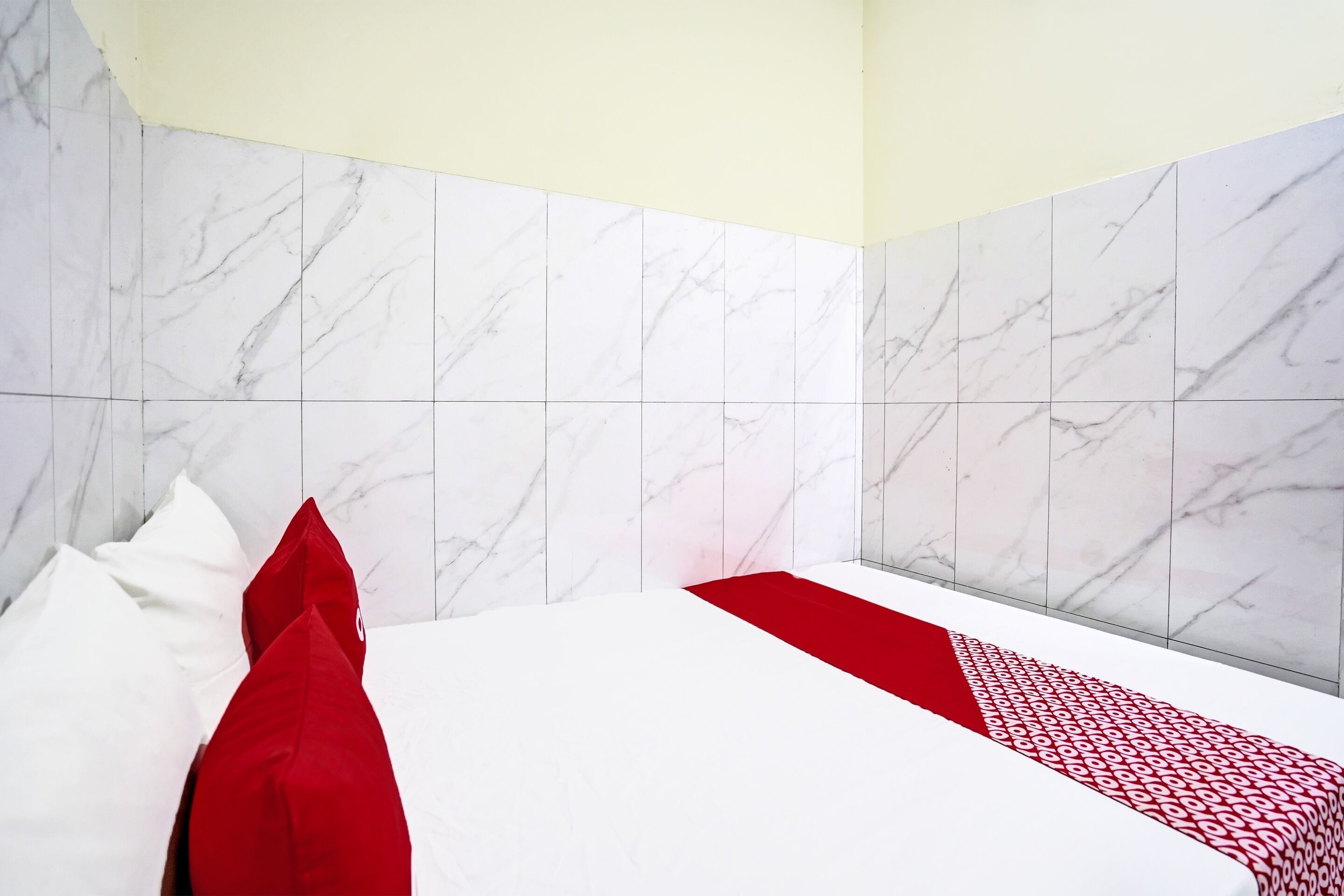 A hotel room with a bed, white and red bedding, and marble-patterned walls.
