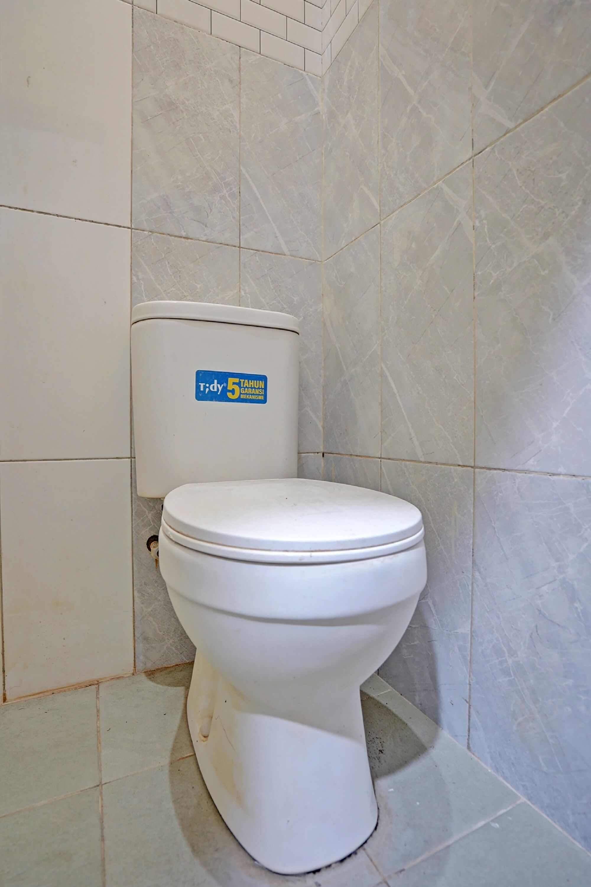 Eine weiße Toilette mit blauem Aufkleber in einem Badezimmer mit gefliesten Wänden und Boden.