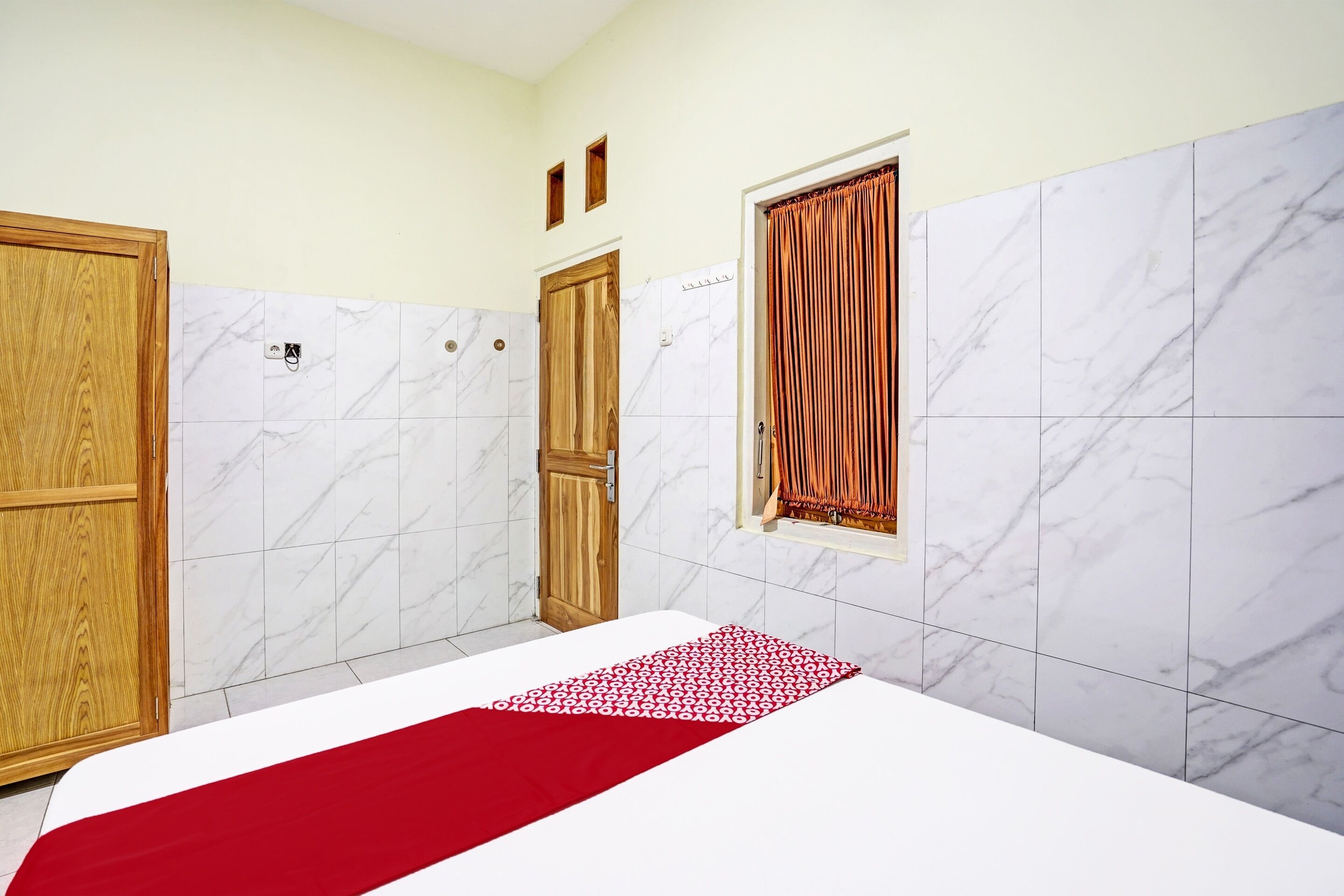 Una habitación de hotel con cama, armario de madera, baño con cortina de ducha y baldosas de mármol.