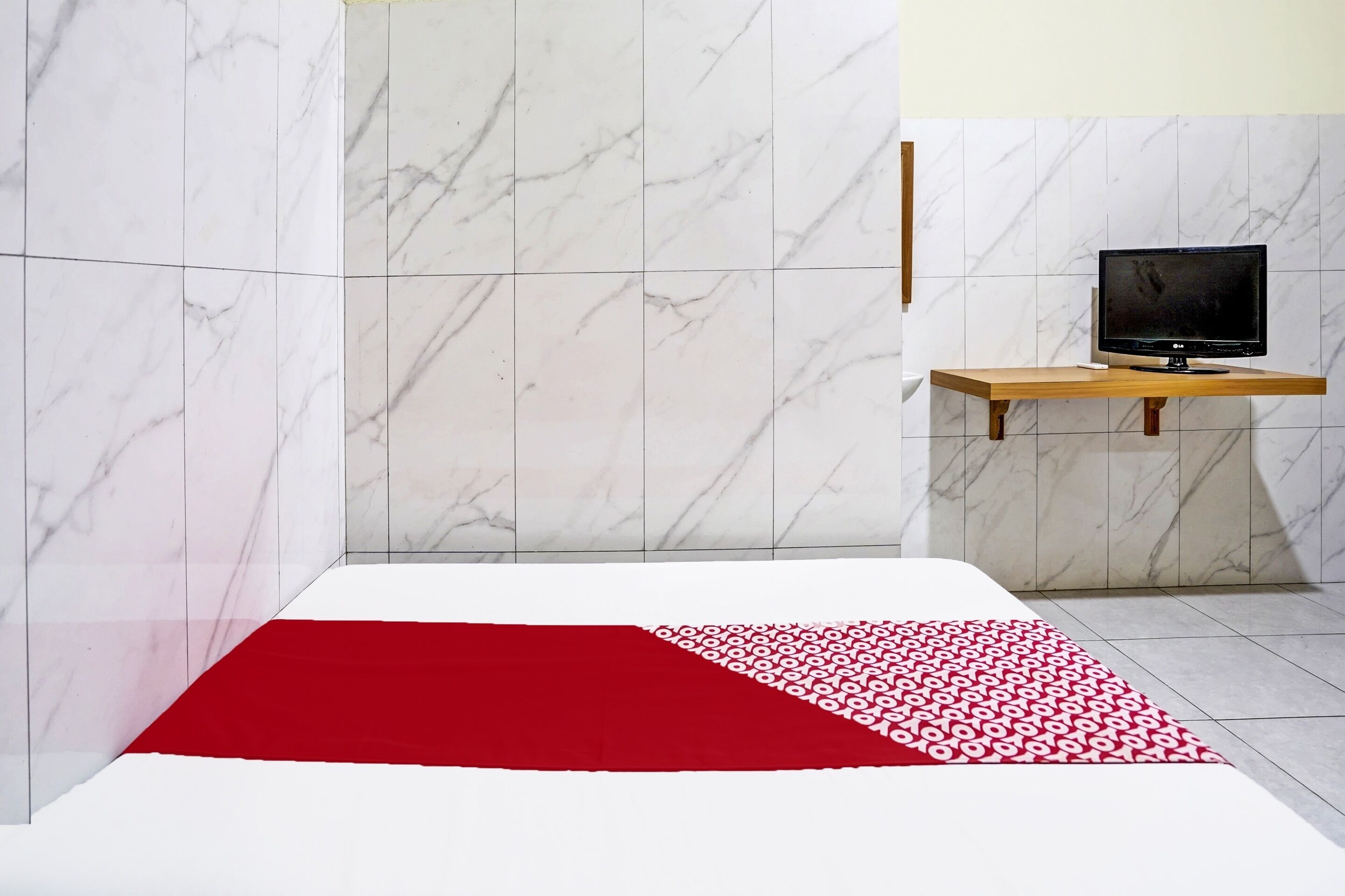 A modern bathroom with marble walls, a wooden shelf holding a television, and a red patterned rug on the floor.