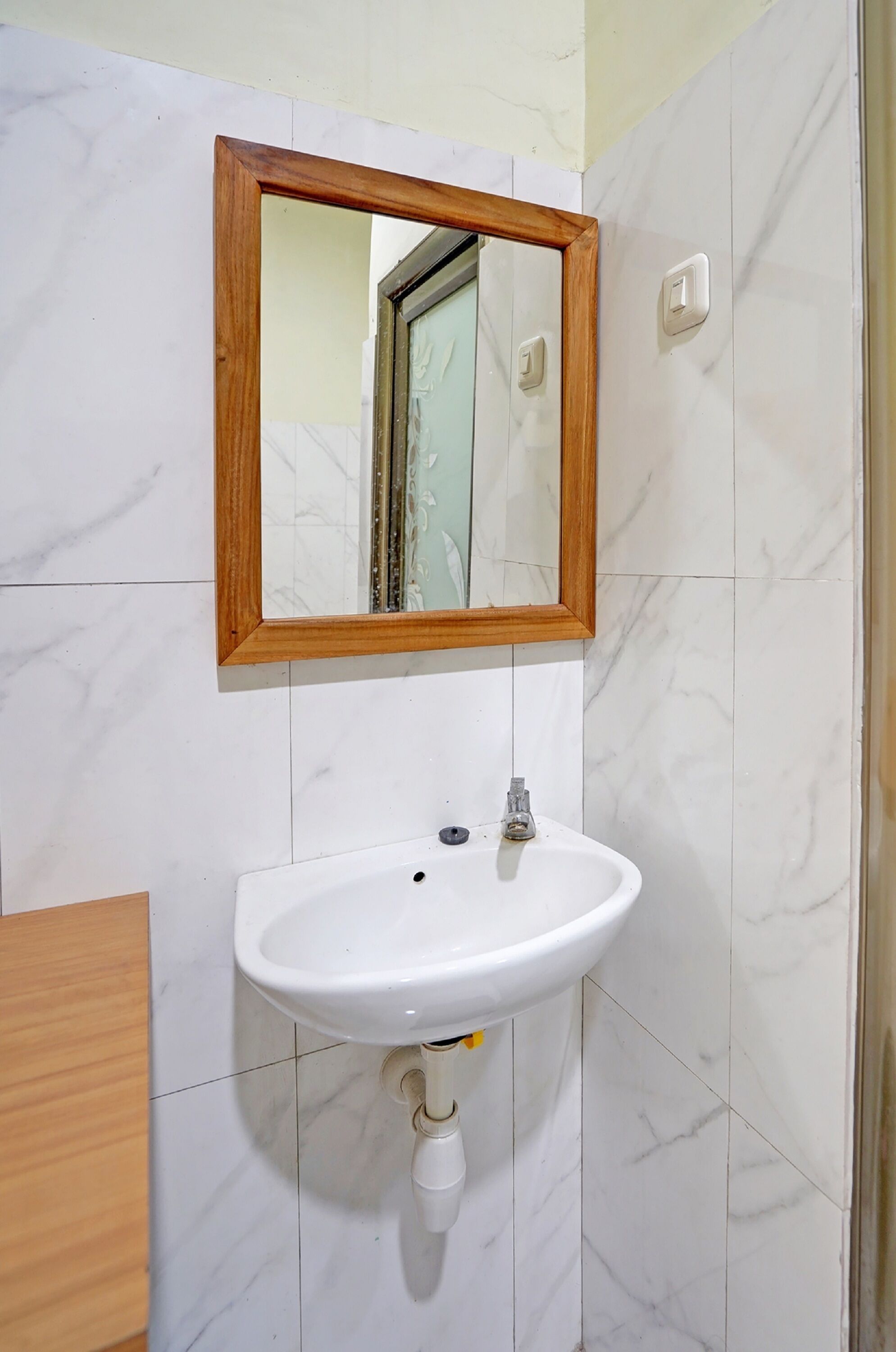 A bathroom with a white sink, wooden frame mirror, and marble tiles.