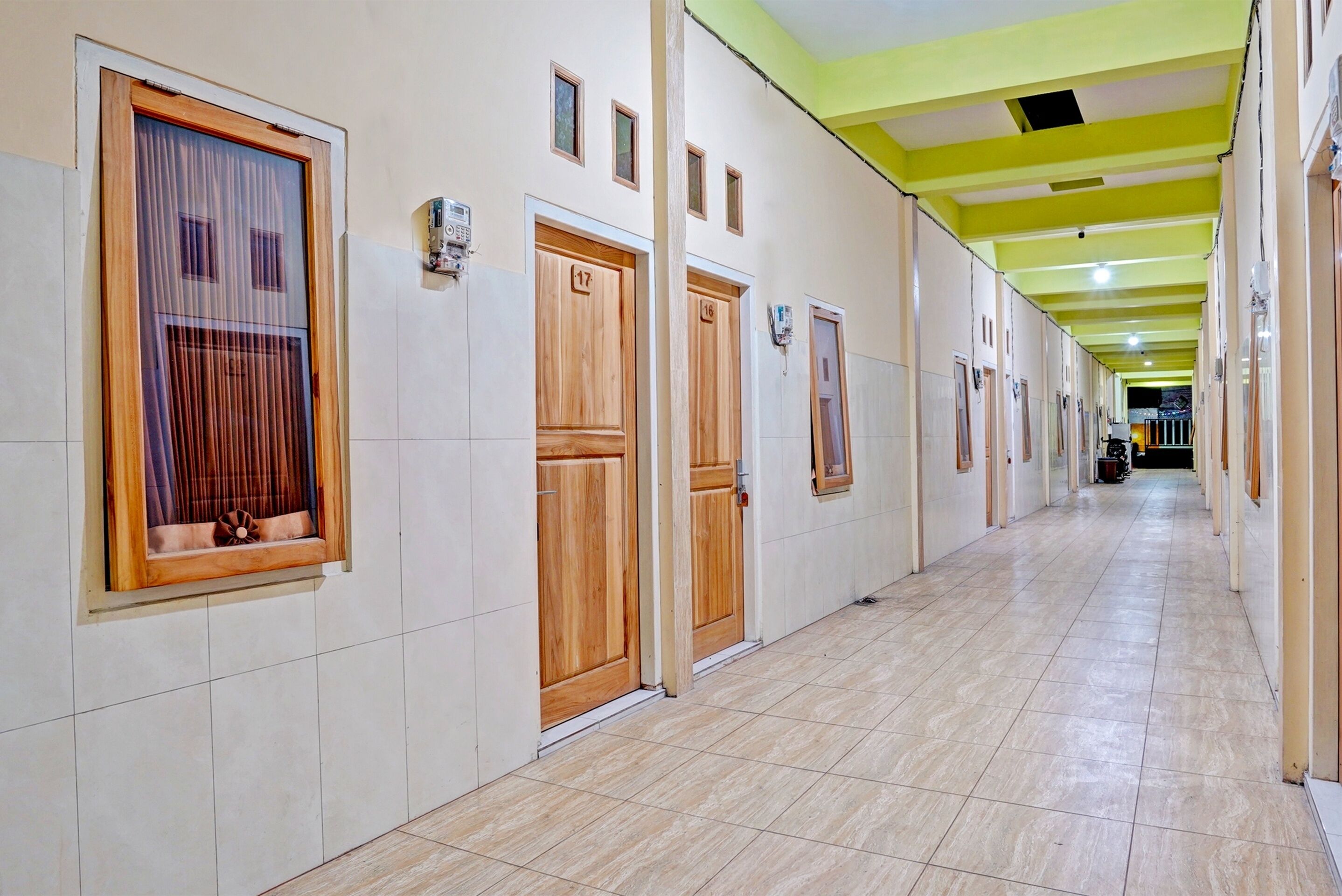 Pasillo de hotel con puertas de madera, placas con números de habitación y suelo de baldosas.