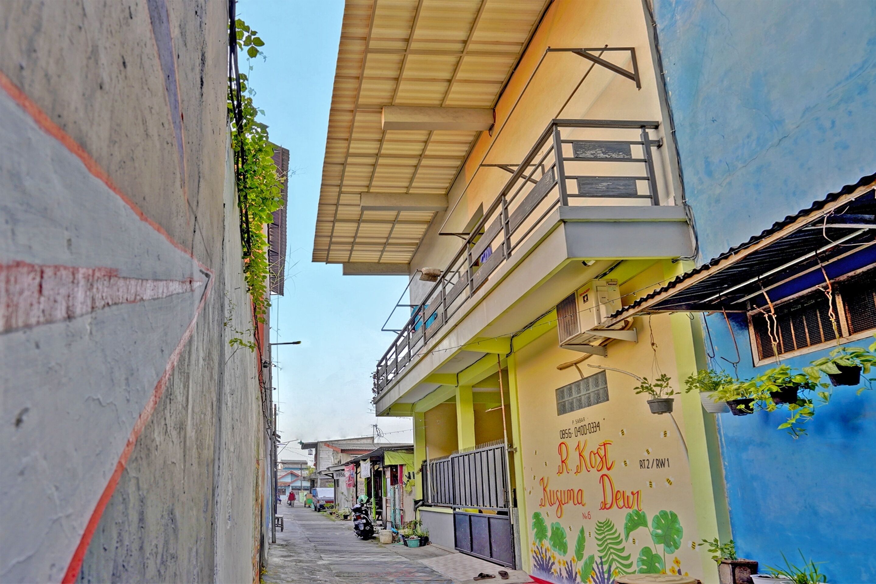 A narrow street with buildings on either side, some with balconies and plants.