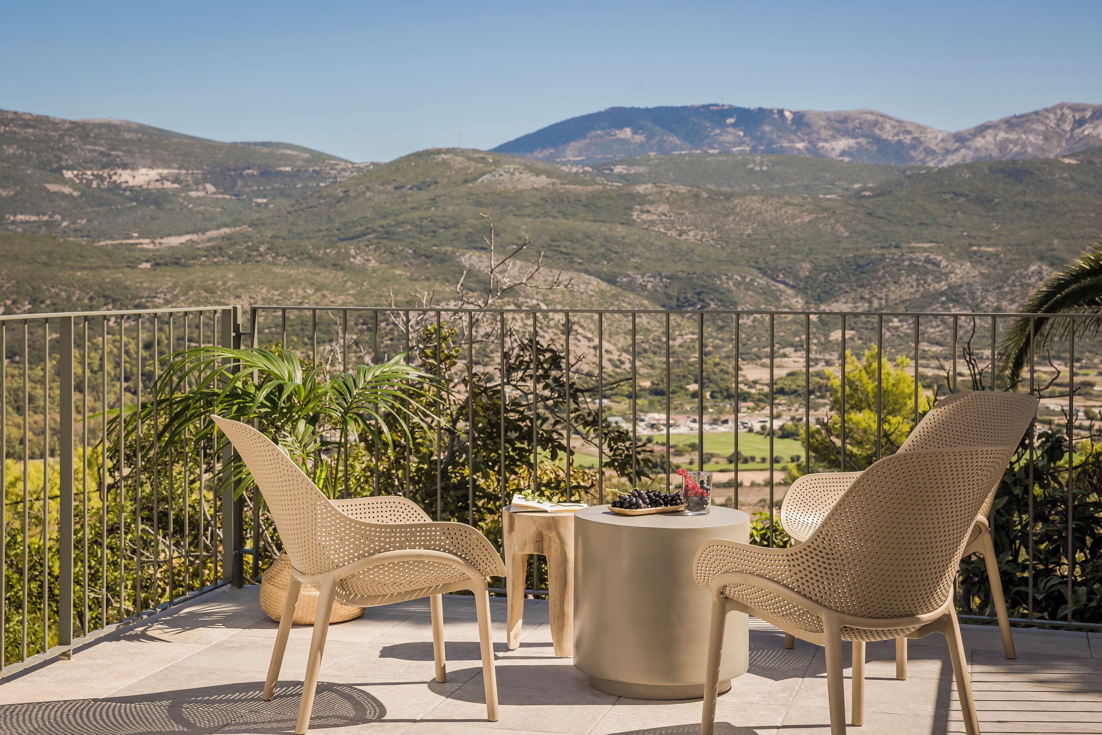 Un balcone con sedie in vimini e un tavolo rotondo, con vista su un paesaggio montuoso.