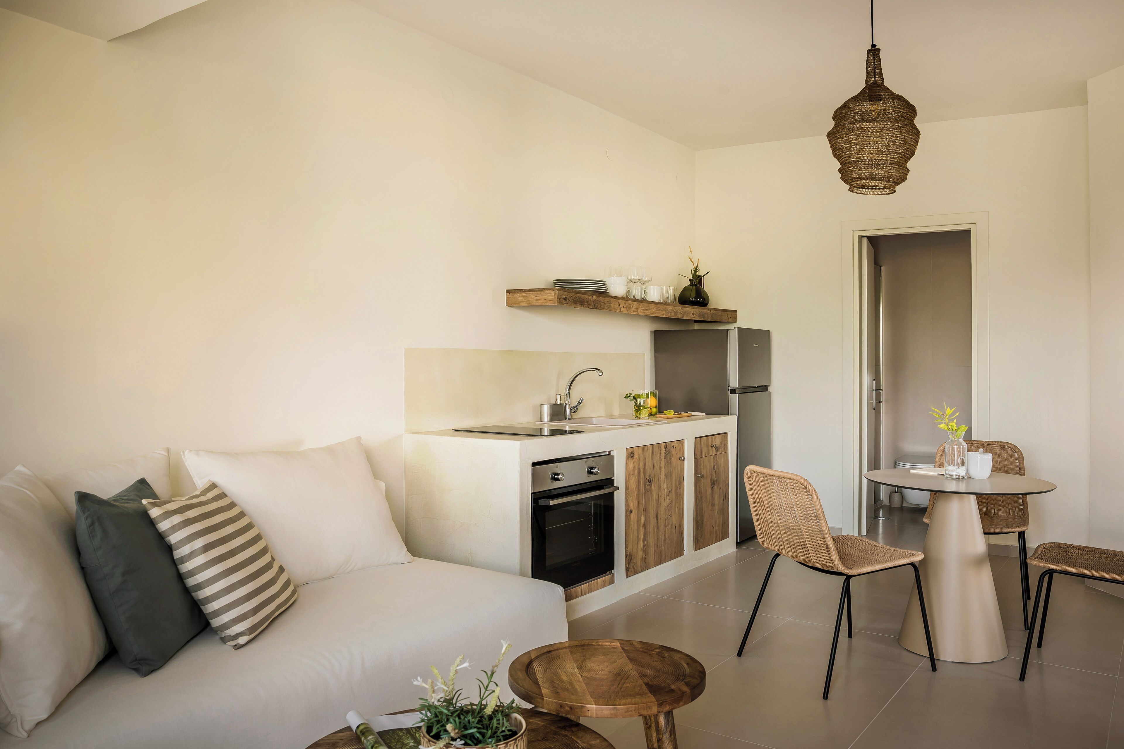 A modern kitchen with a built-in oven, a dining area with a round table and chairs, and a living area with a sofa and cushions.