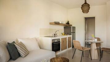 A modern kitchen with a built-in oven, a dining area with a round table and chairs, and a living area with a sofa and cushions.