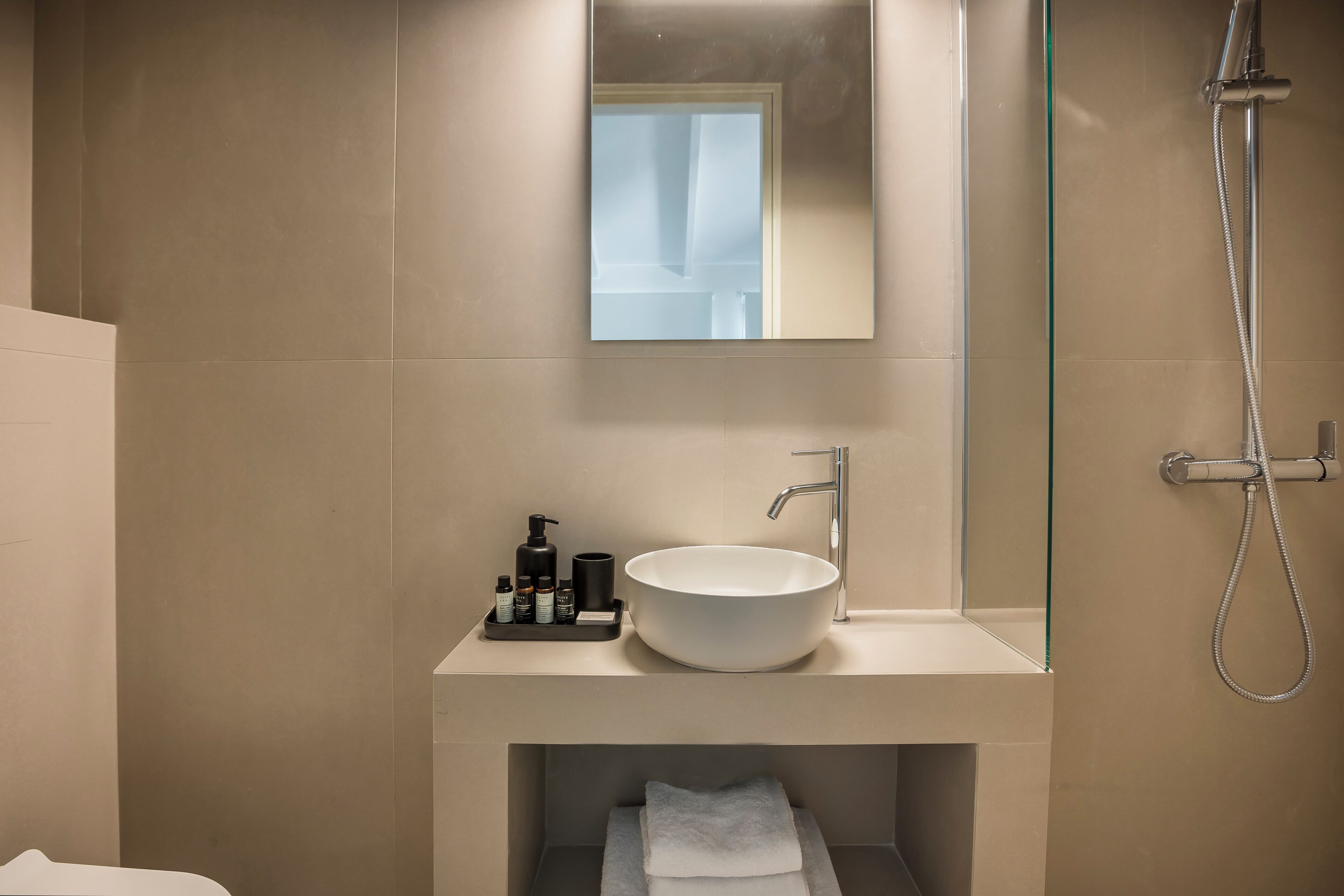 A modern bathroom with a large white sink, a mirror, and a shower.