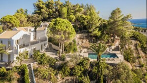 Una villa con piscina, rodeada de árboles y vista al mar.