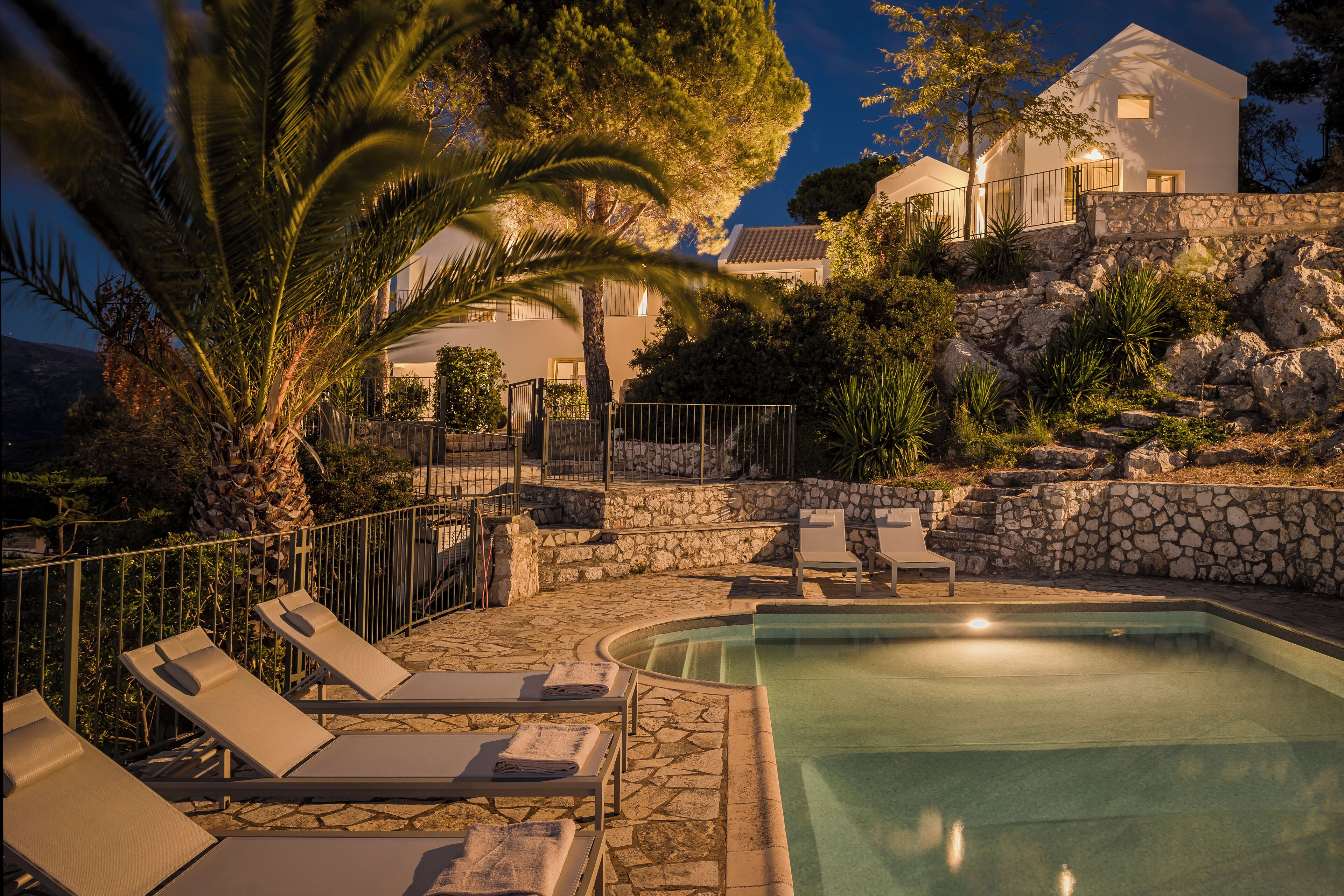 A pool area with lounge chairs, a stone wall, and a building in the background.