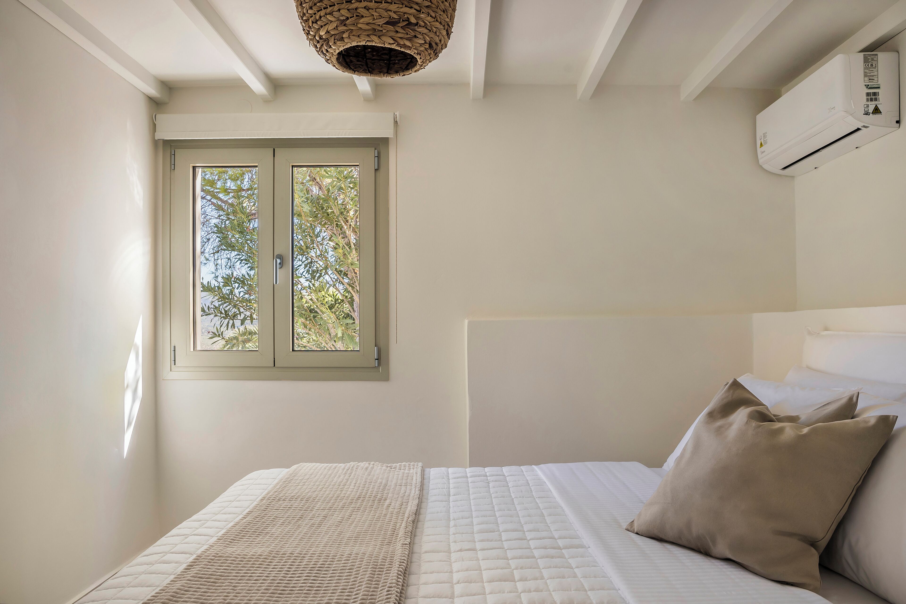 Ein Schlafzimmer mit Bett, Fenster, Klimaanlage und einer gewebten Deckenleuchte.