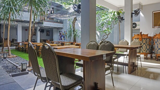 A spacious indoor dining area with wooden tables and patterned chairs, surrounded by greenery and a balcony. - Capital O 91140 Ayodya Kebon Jeruk (Jakarta)