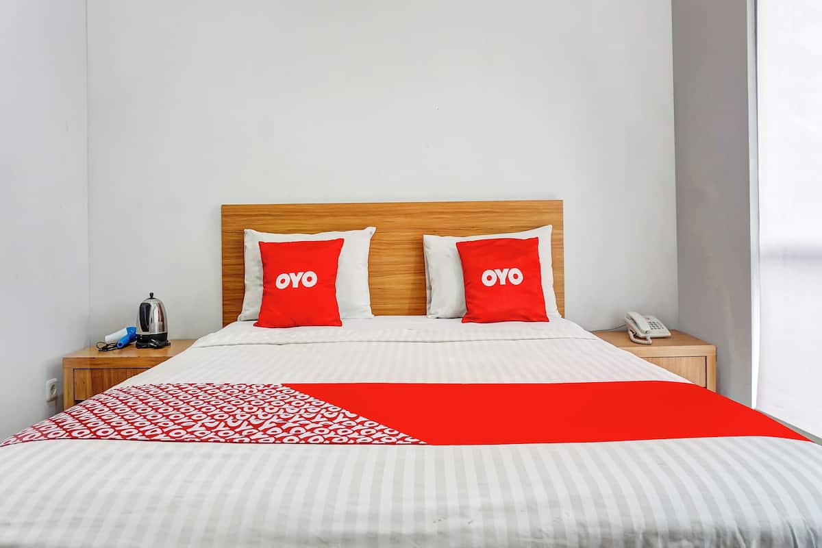 A bed with two red pillows, a wooden headboard, a white and red striped bedspread, a bedside table with a phone, and a kettle.