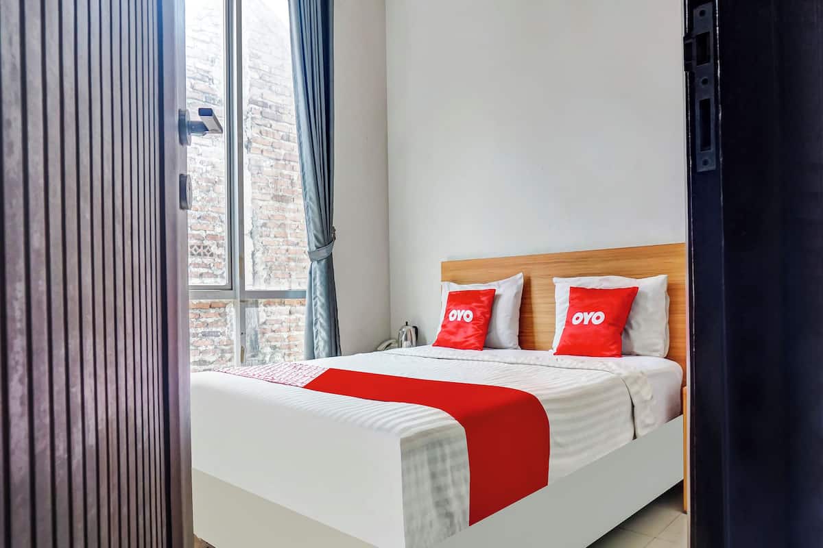 A neatly made bed with white and red bedding, a wooden headboard, and two pillows with "OYO" branding.