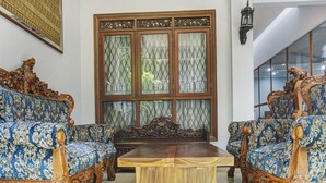A room with ornate blue patterned sofas, a wooden coffee table, and a large window with decorative glass panels. - Capital O 91140 Ayodya Kebon Jeruk (Jakarta)