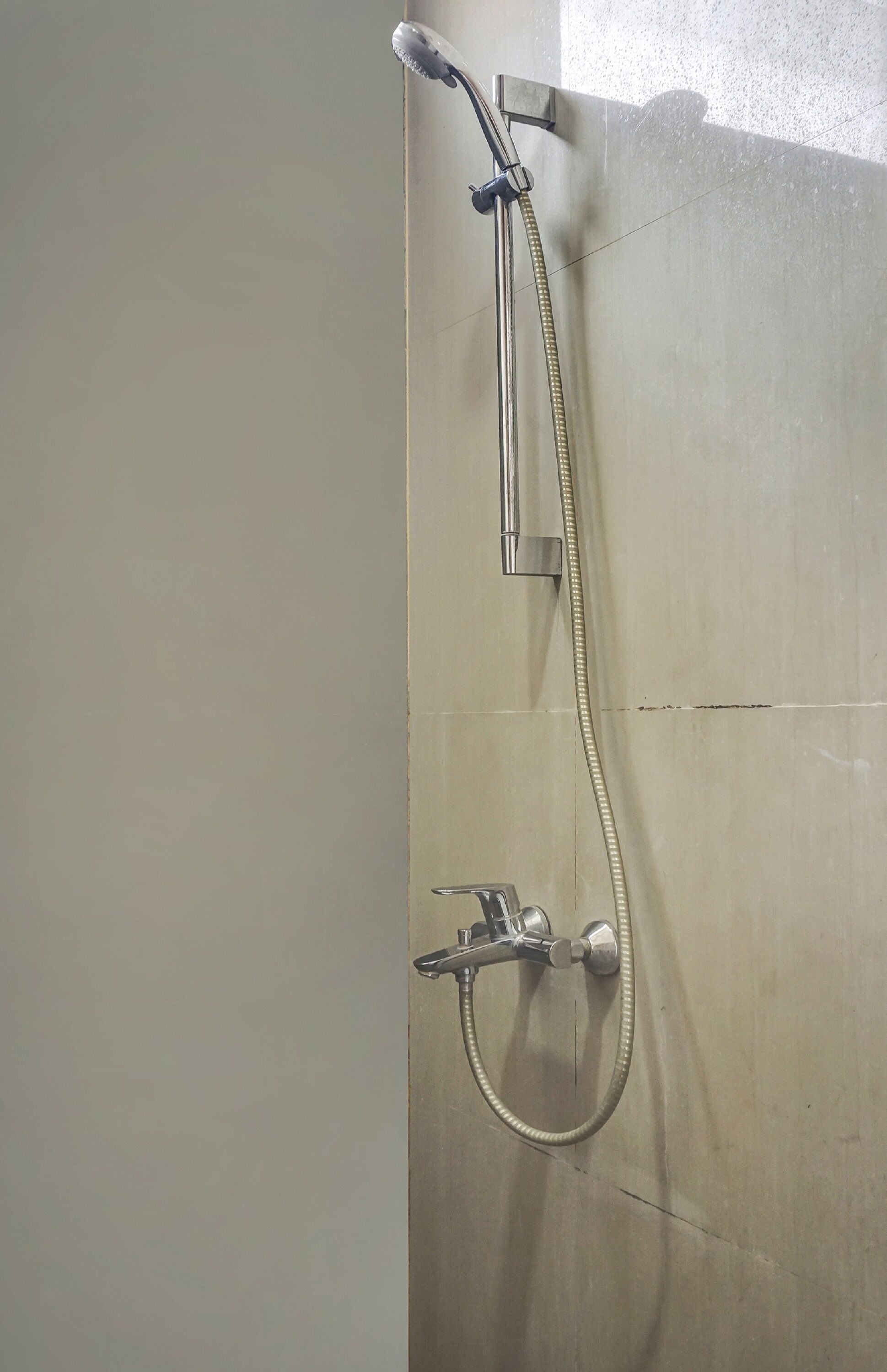 Ducha con cabezal de ducha manual y cabezal fijo, montada en una pared con azulejos.