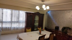 Ein Esszimmer mit rundem Tisch, Stühlen, einer Kandelaber und einem großen Fenster mit Vorhängen.