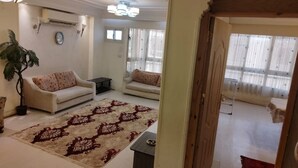 Ein Wohnzimmer mit einer Couch, einem Couchtisch und einem gemusterten Teppich. Eine Tür führt in einen anderen Raum.
