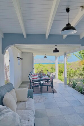 Une terrasse couverte avec une table et des chaises, un canapé et une vue sur la mer.