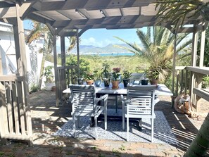 Un patio techado con una mesa y sillas, rodeado de plantas en macetas y vistas a montañas.