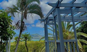 Une structure de pergola en bois offrant une vue sur un paysage côtier, avec des palmiers et une montagne lointaine.