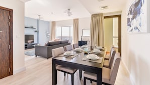 A modern dining area with a long table set for six, a gray sofa, and a city view through large windows. - Luxury JBR Shams - Sea or Marina View - Free Beach Resorts Access! (Dubai)