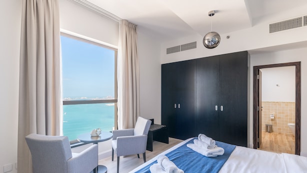 A hotel room with a bed, two chairs, a small table, a wardrobe, and a view of the sea. - Luxury JBR Shams - Sea or Marina View - Free Beach Resorts Access! (Dubai)