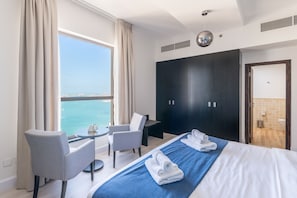 A hotel room with a bed, two chairs, a small table, a wardrobe, and a view of the sea.