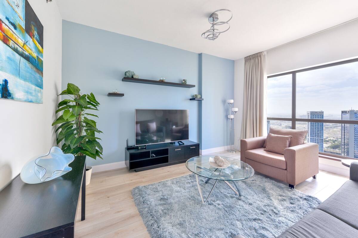 Ein modernes Wohnzimmer mit Flachbildfernseher, einer Couch, einem Glastisch und einem großen Fenster mit Blick auf die Stadt.