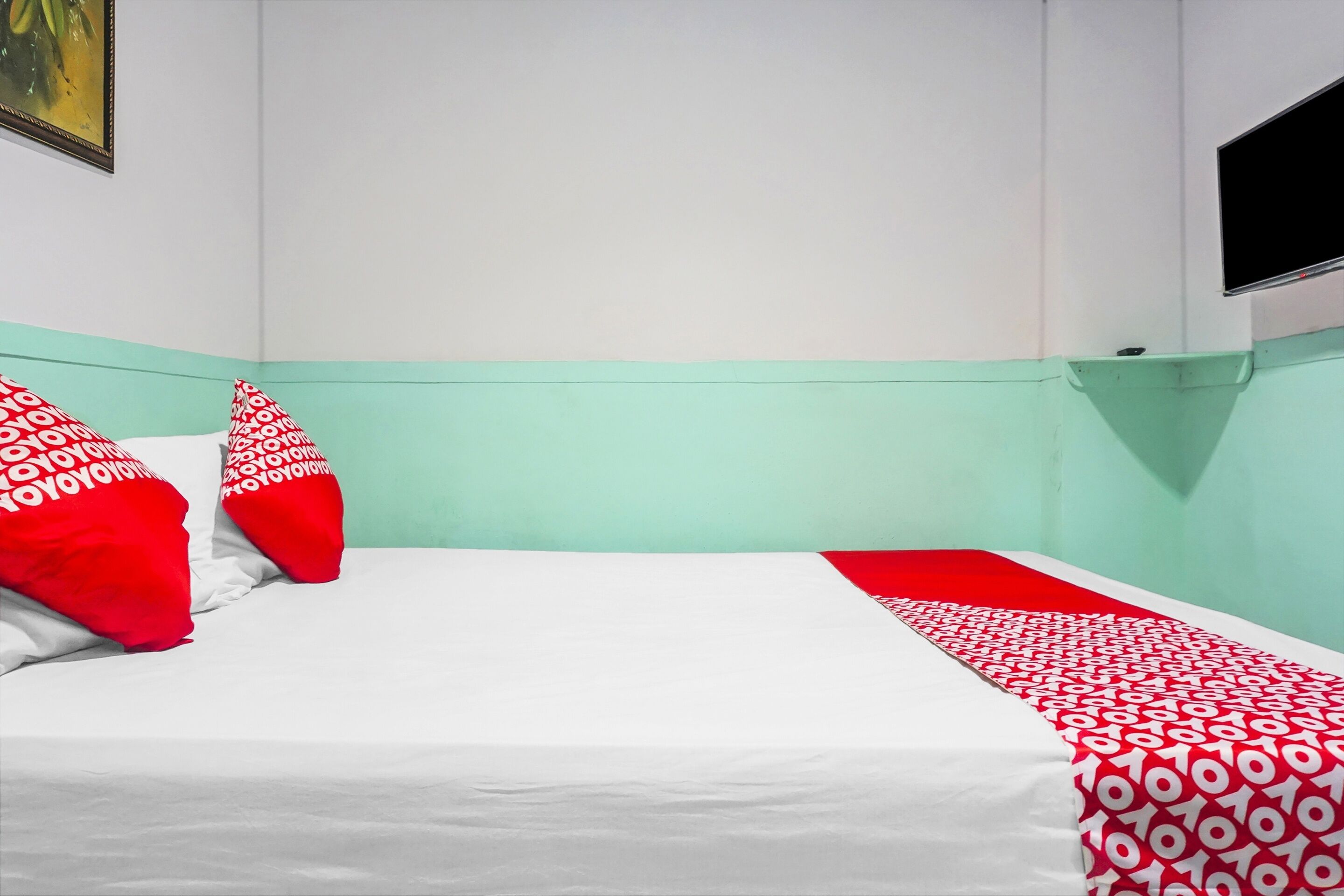 A hotel room with a bed, red and white patterned pillows, a red and white bedspread, and a television mounted on the wall.