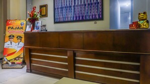 A hotel reception desk with a wooden counter, a framed abstract painting, and a Maneki-neko statue.