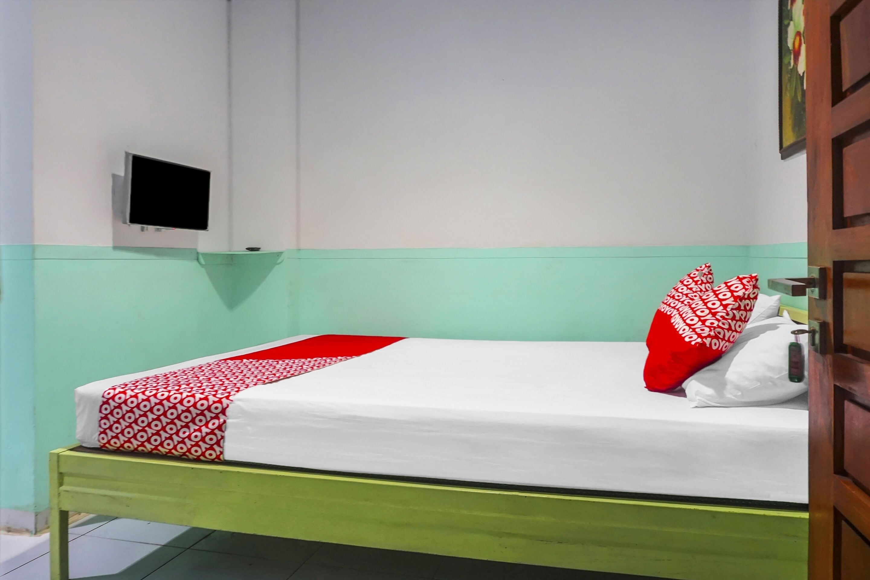 Een eenpersoonsbed met een bedovertrek met patroon, een rood-wit kussen en een wit kussen op een groen metalen frame.