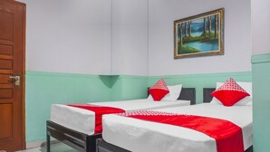 A hotel room with two beds, each with white bedding and red pillows, a wooden door, and a painting of a forest scene on the wall.