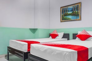 A room with two beds, each with white bedding and red accents, a painting on the wall, and a green accent wall.