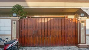 A gated entrance with a wooden gate, a motorcycle parked to the left, and a building with a balcony and a staircase. - OYO 91316 Hh Guest House Makassar (Makassar)
