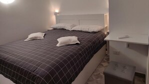Quarto com cama, duas almofadas, mesa de cabeceira e criado-mudo.