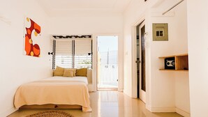 Ein Schlafzimmer mit einem Bett, einem gewebten Teppich, einer Tür mit Schlüsselloch und einem Wandbild mit geometrischen Mustern.
