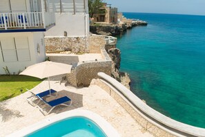 A pool area with a stone deck, lounge chairs, and a view of the sea.