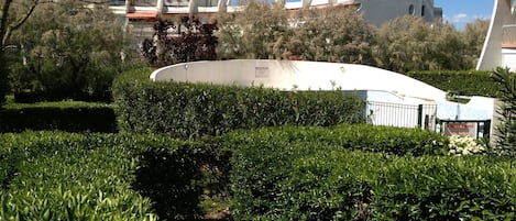 Een aangelegde tuin met een gebogen pad, een wit gebouw met een bijzonder architectuur en een bordje dat een vaccinatiecentrum aangeeft.