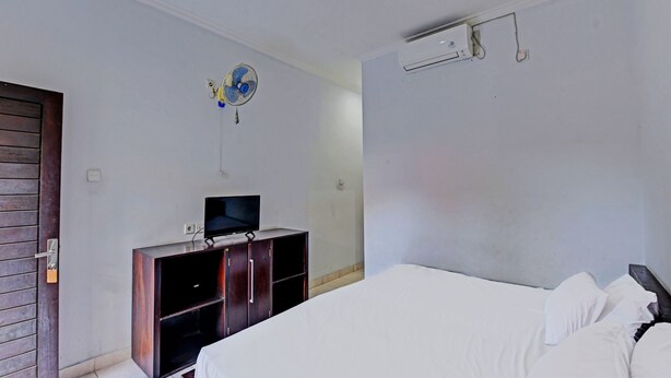 Une chambre à coucher avec un lit, un téléviseur posé sur un meuble en bois, un ventilateur de plafond et un appareil de climatisation.