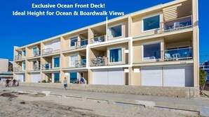 Un immeuble à plusieurs étages doté de balcons et de grandes fenêtres, présenté comme une terrasse exclusive en bord de mer, offrant une vue idéale sur l’océan et la promenade.