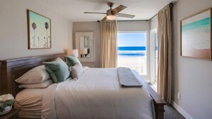 Une chambre d’hôtel avec un lit, un ventilateur de plafond, une vue sur la plage et une fenêtre avec des rideaux.