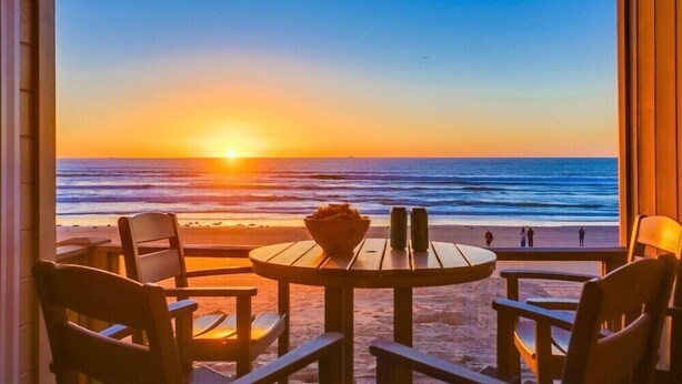 Une table et des chaises placées face à une plage, avec vue sur le coucher de soleil.