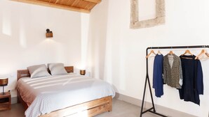 A bedroom with a wooden bed, a bedside table, a wall-mounted light, and a clothing rack with hangers. - Ammonite Lodge, Pic Saint Loup (Vacquières)